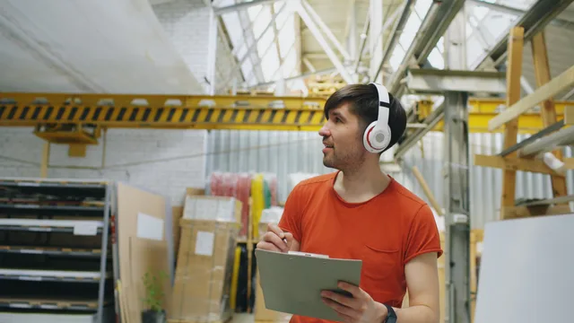 Young adult warehouse worker wearing headphones while taking inventory indoors. Kostnadsposter att budgetera för en e-handelsbutik